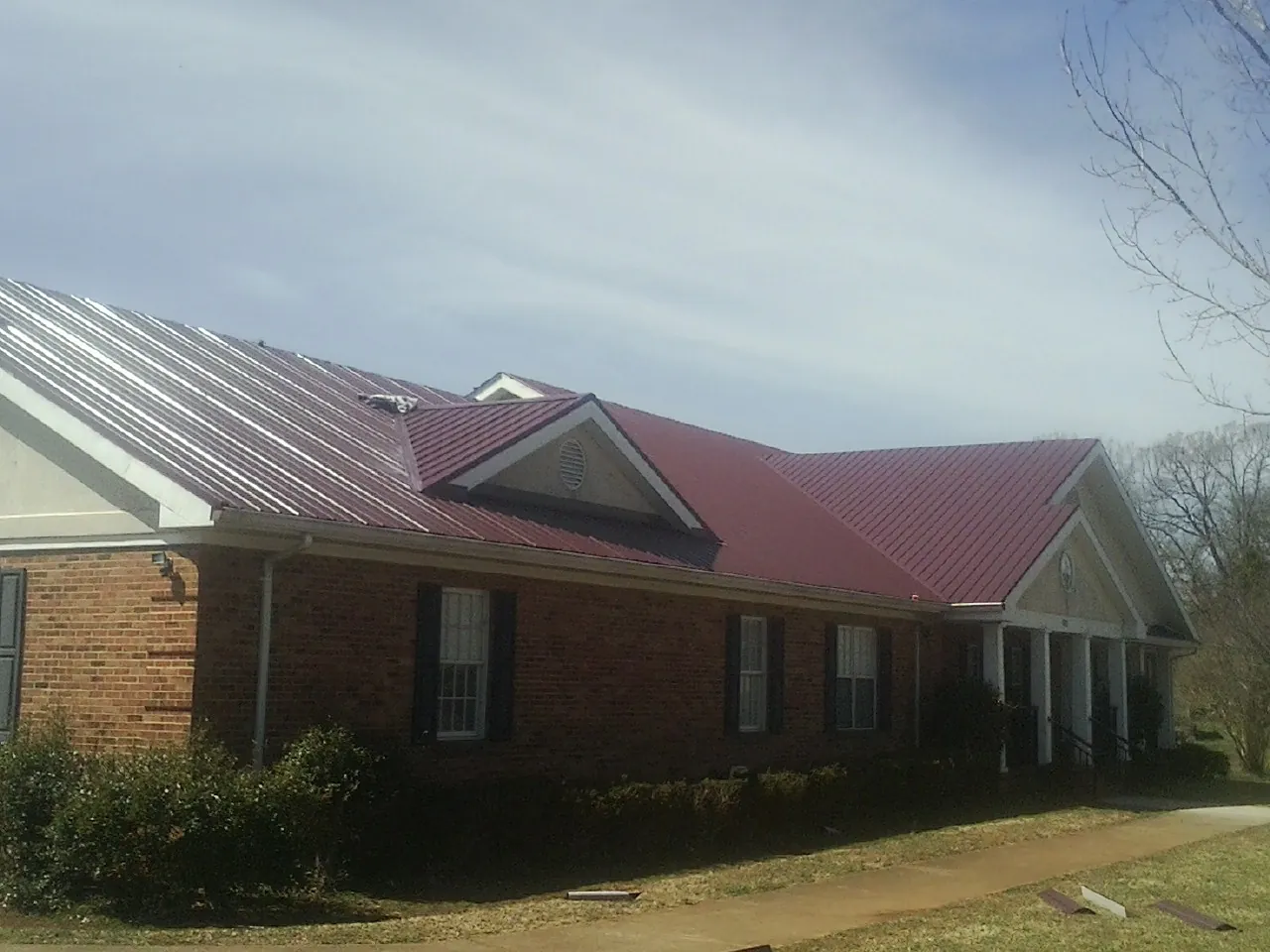 Red metal roof with gabled entries on a long brick building, from a Hail Damage Roof Repair job in Cove City