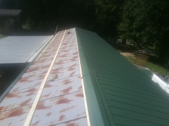 Old rusted panels beside newly installed green metal roofing — Wind Damage Roof Repair by Roofing Brothers in Cove City