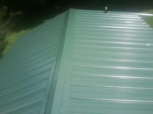 New green metal panels meeting at the ridge of a roof — Flat Roof Repair work by our crew in Cove City