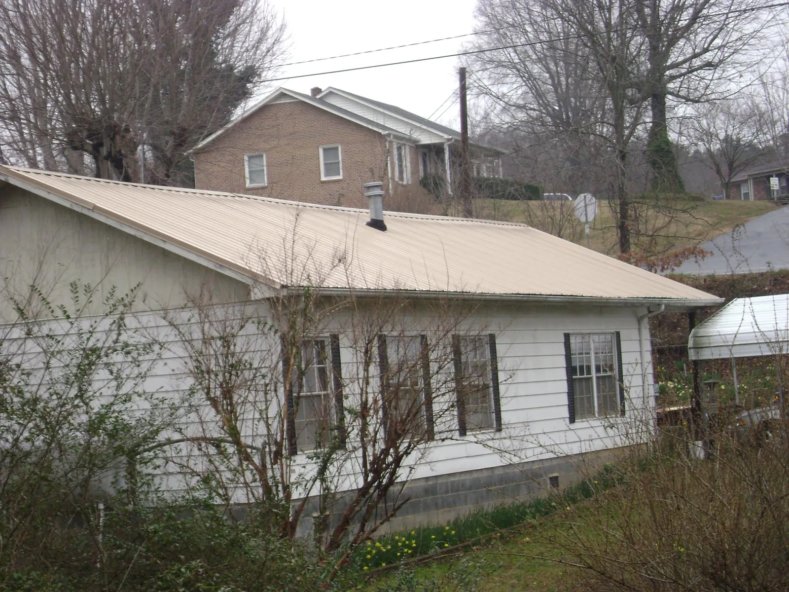 Tan metal roof on a white sided house set into a hillside — Commercial Roofing by Roofing Brothers in Cove City