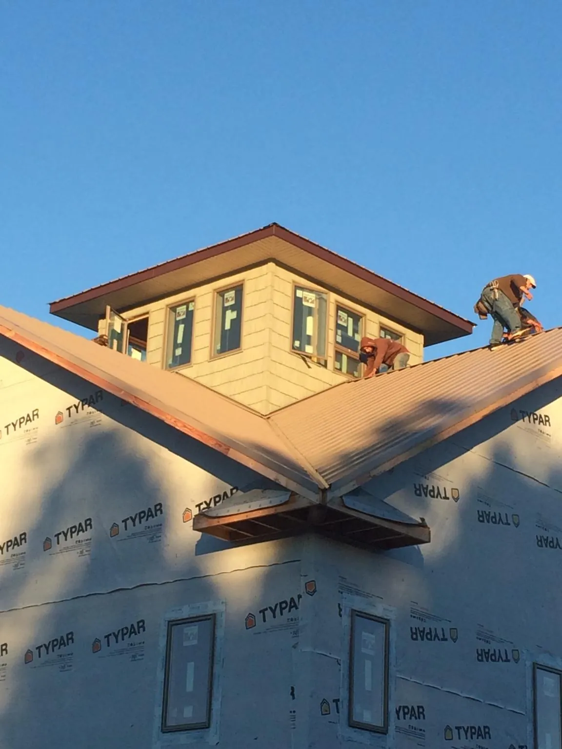 Roofers working around a rooftop cupola on a new metal roof at sunset — Roof Waterproofing in Cove City by Roofing Brothers